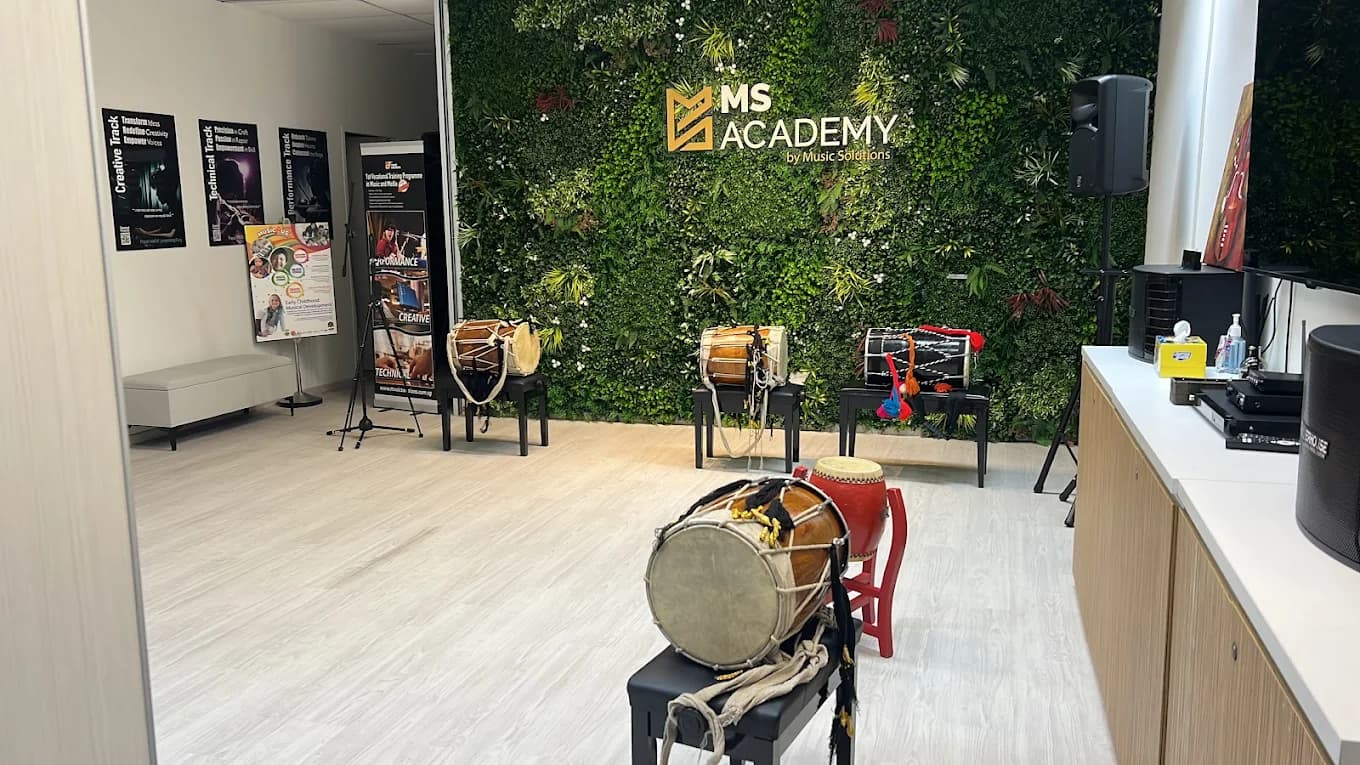 MS Academy reception lobby with a green living-wall feature bearing the MS Academy logo and hand-percussion drums displayed on stands