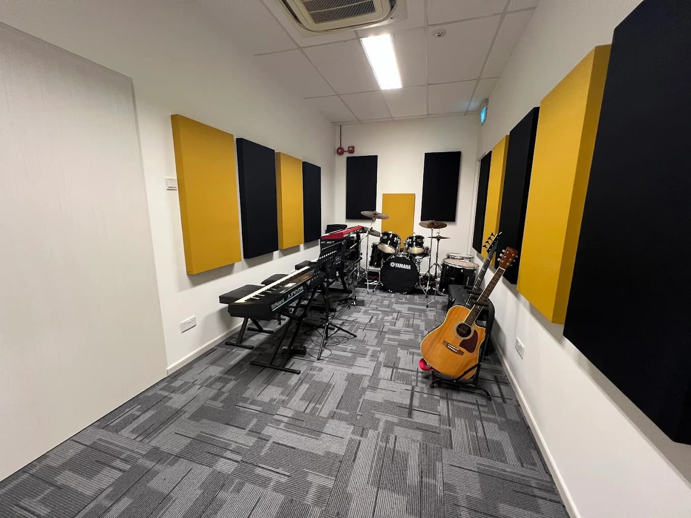 Band room lined with yellow and black acoustic panels, containing a drum kit, a keyboard on a stand and an acoustic guitar