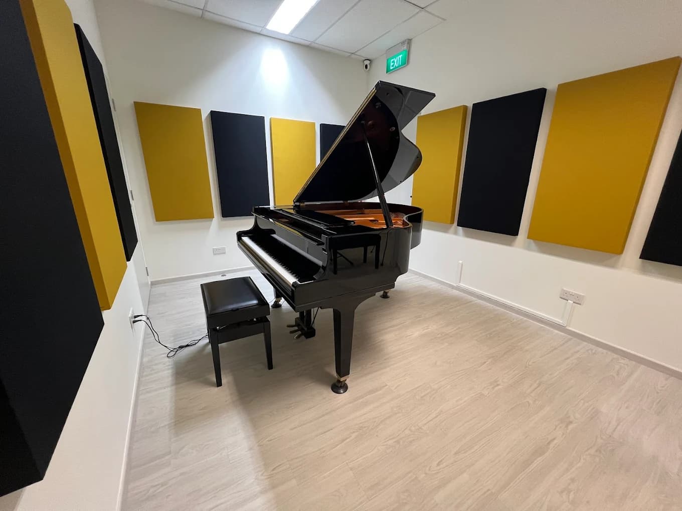 Small acoustic-treated room with yellow and black sound panels, a black grand piano and matching bench