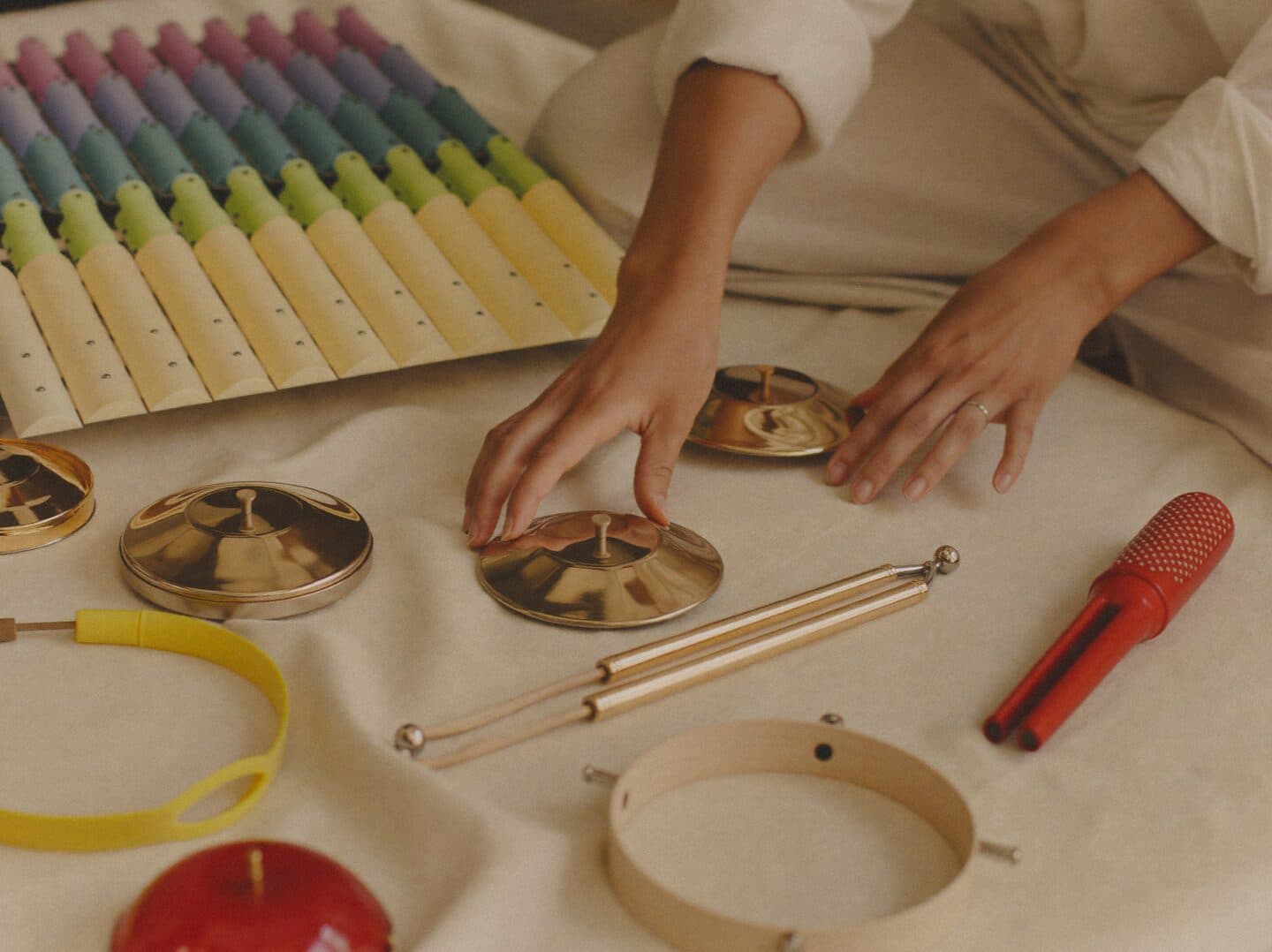 Hands exploring a set of colourful accessible percussion instruments — a pastel xylophone, finger cymbals and chimes