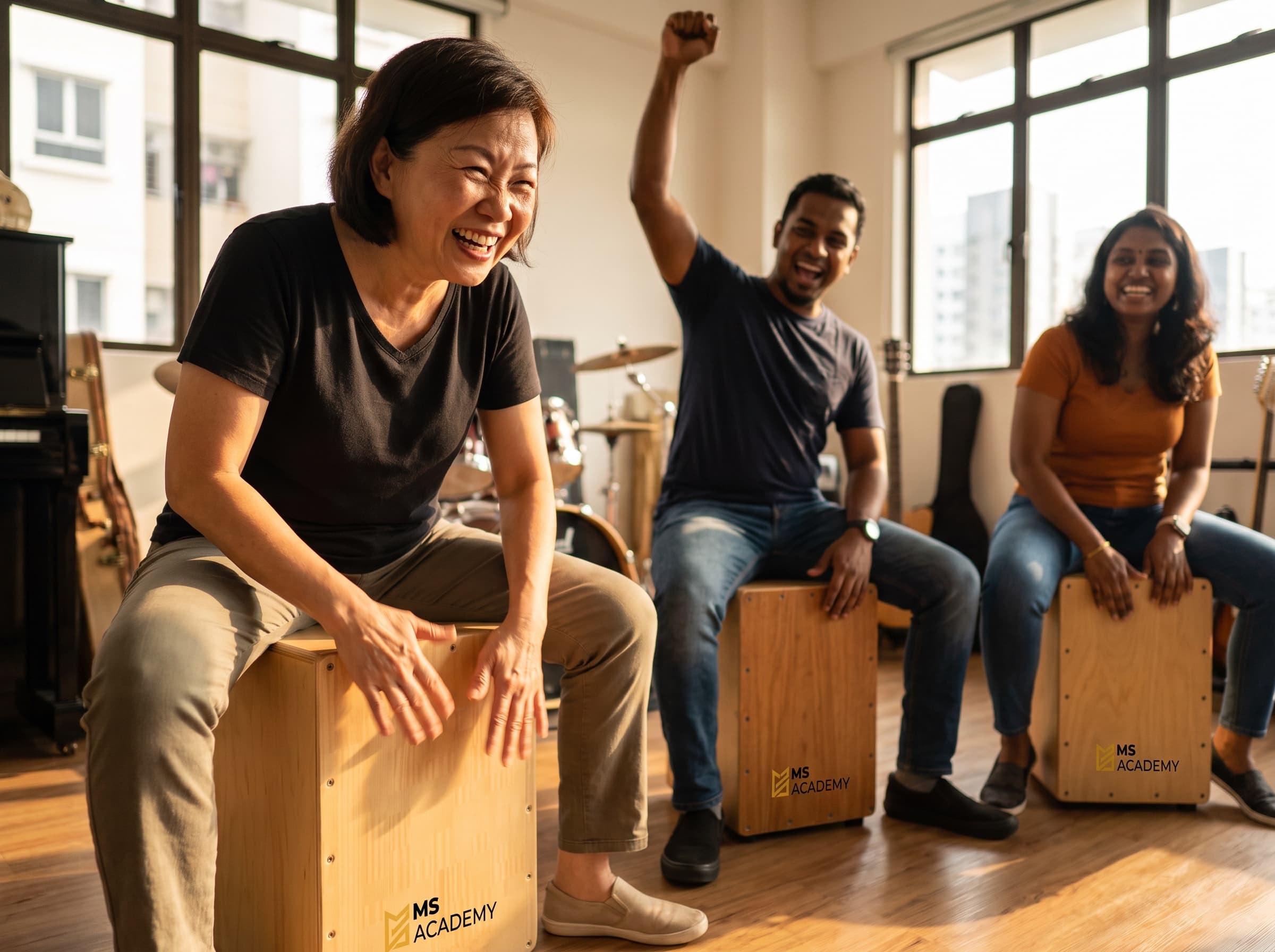 Caregivers drumming on MS Academy cajons during a Shout-Out Cajon session — one mid-beat laughing, another cheering with a fist in the air
